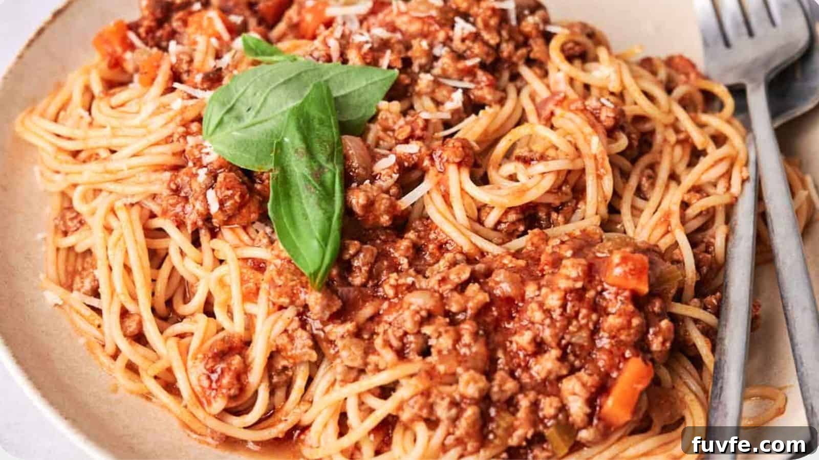 A plate of spaghetti topped with meat sauce and a fresh basil leaf, accompanied by a fork on the side.