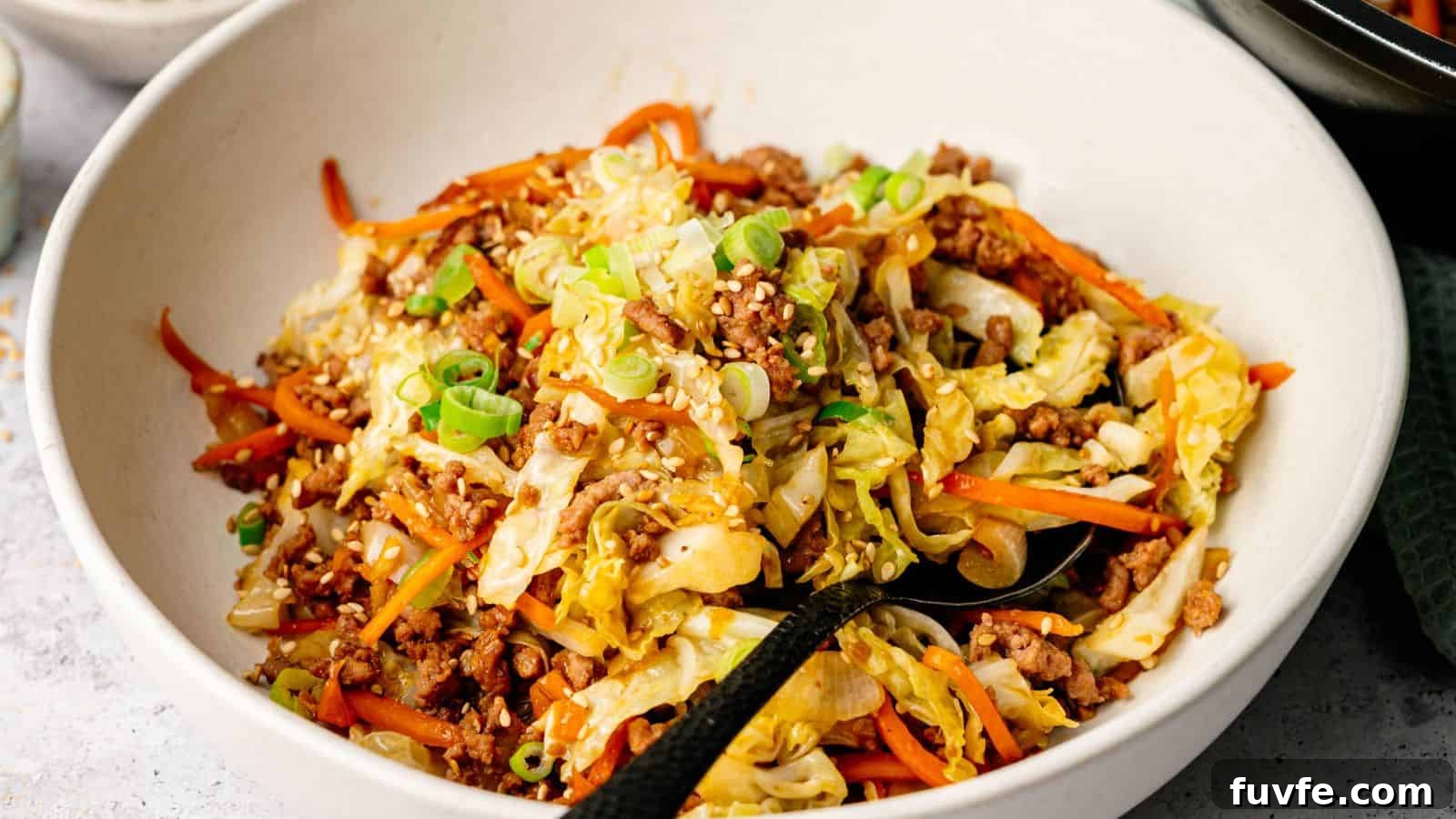 A bowl of stir-fried ground meat, shredded cabbage, and carrots, topped with sesame seeds and chopped green onions.