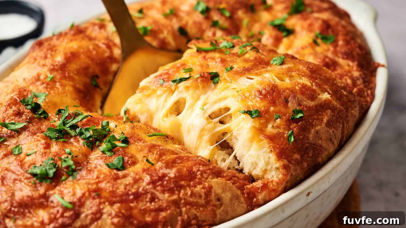 A golden-brown baked dish with melted cheese and chopped herbs, being served with a spoon from an oval white casserole dish.