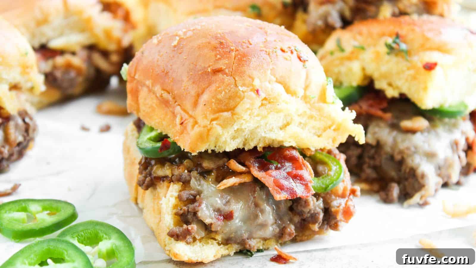 A close-up of sliders filled with cooked ground beef, melted cheese, bacon, and sliced jalapeños on a white surface, with some jalapeño slices scattered nearby.