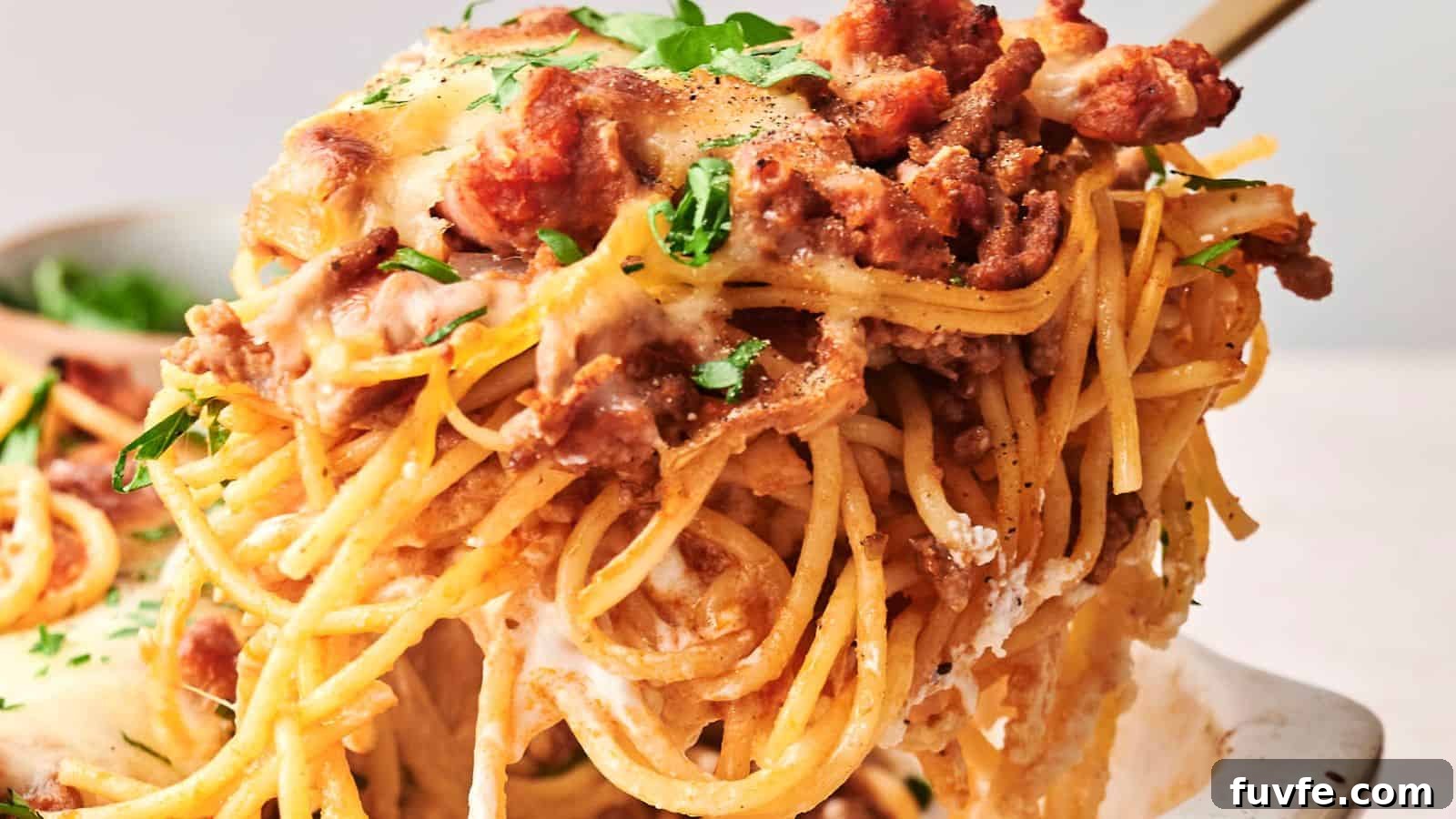 Close-up of a serving of cheesy baked spaghetti with meat sauce, topped with fresh parsley, being lifted from a dish.