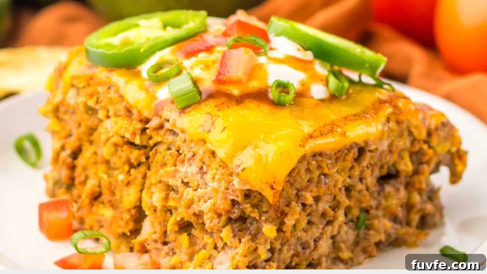 Close-up of a slice of cheesy taco casserole topped with chopped tomatoes, green onions, and jalapeño slices on a white plate, reminiscent of the comforting flavors found in slow cooker taco meatloaf.
