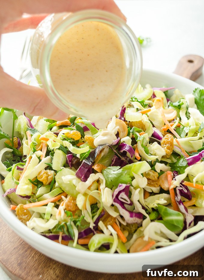 Curried coleslaw dressing pouring over bowl of coleslaw