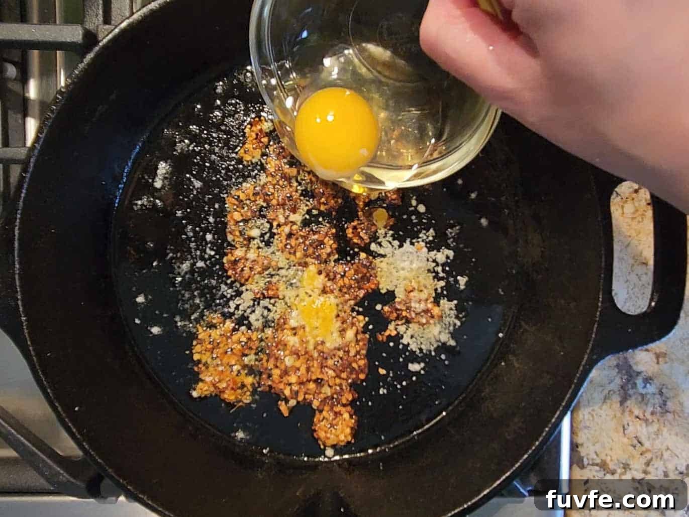 Parmesan Chili Crisp Fried Eggs: Crispy Sunny-Side with Heat 6 An egg is poured into a hot skillet for frying with spices.