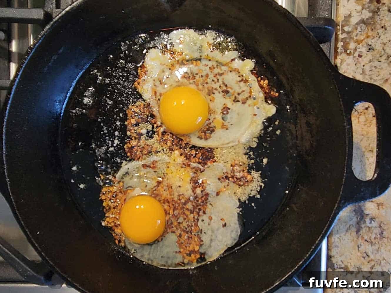 Parmesan Chili Crisp Fried Eggs: Crispy Sunny-Side with Heat 7 Two eggs frying in a hot skillet with spices.