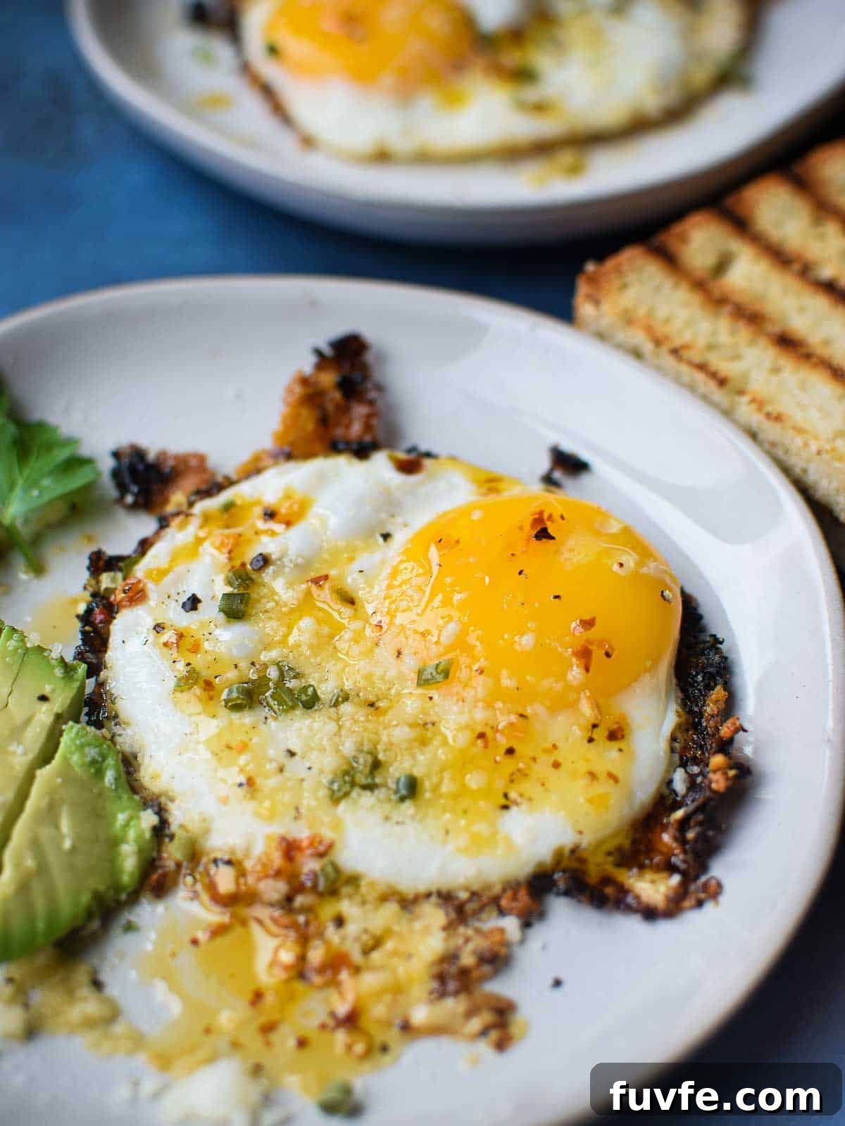 Parmesan Chili Crisp Fried Eggs: Crispy Sunny-Side with Heat 8 Fried egg on a white plate with chili crisp on top.