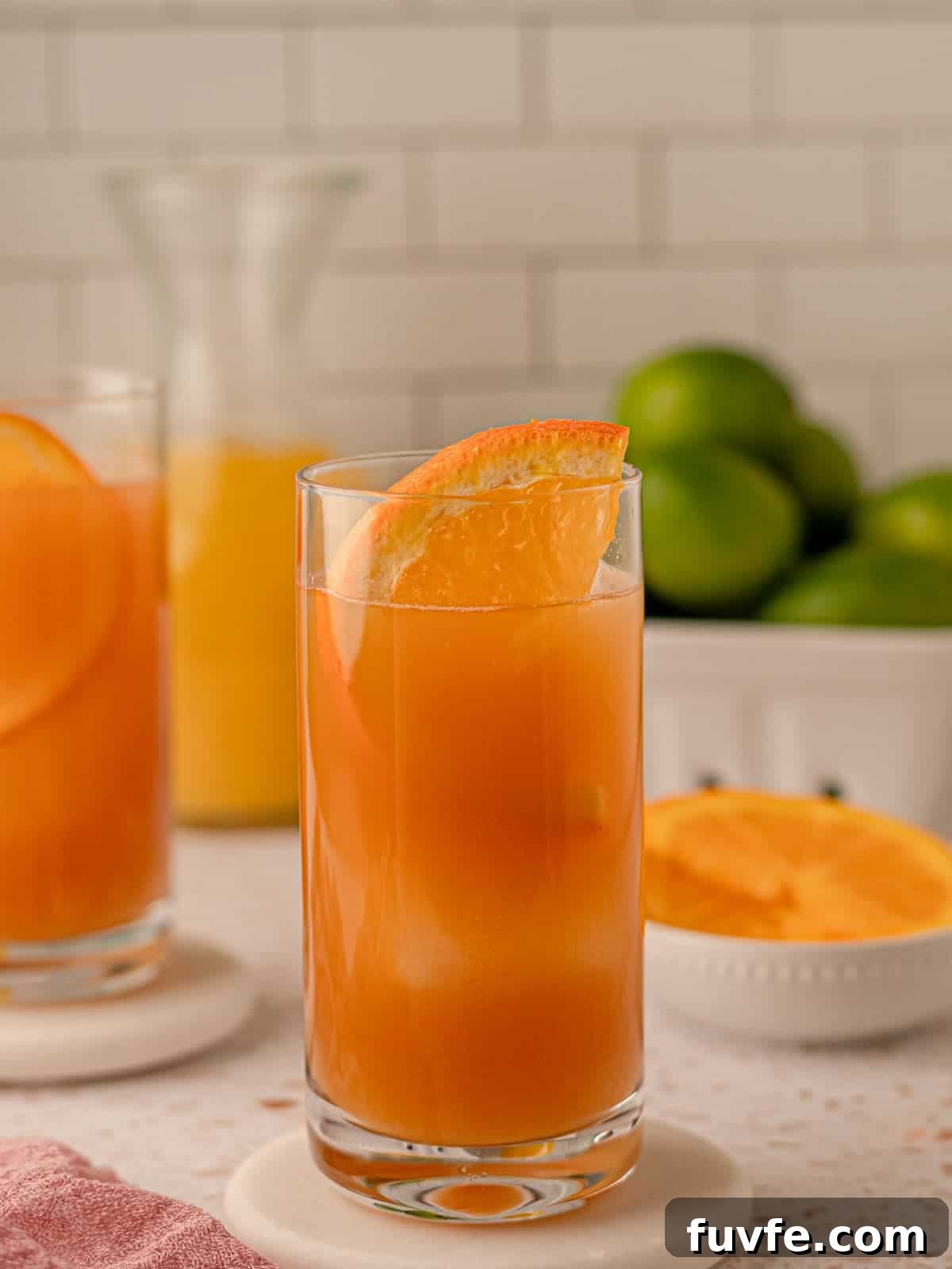 Authentic Jamaican Rum Punch Recipe for Tropical Cocktails 6 A cocktail in a highball glass in front of a bowl of limes.