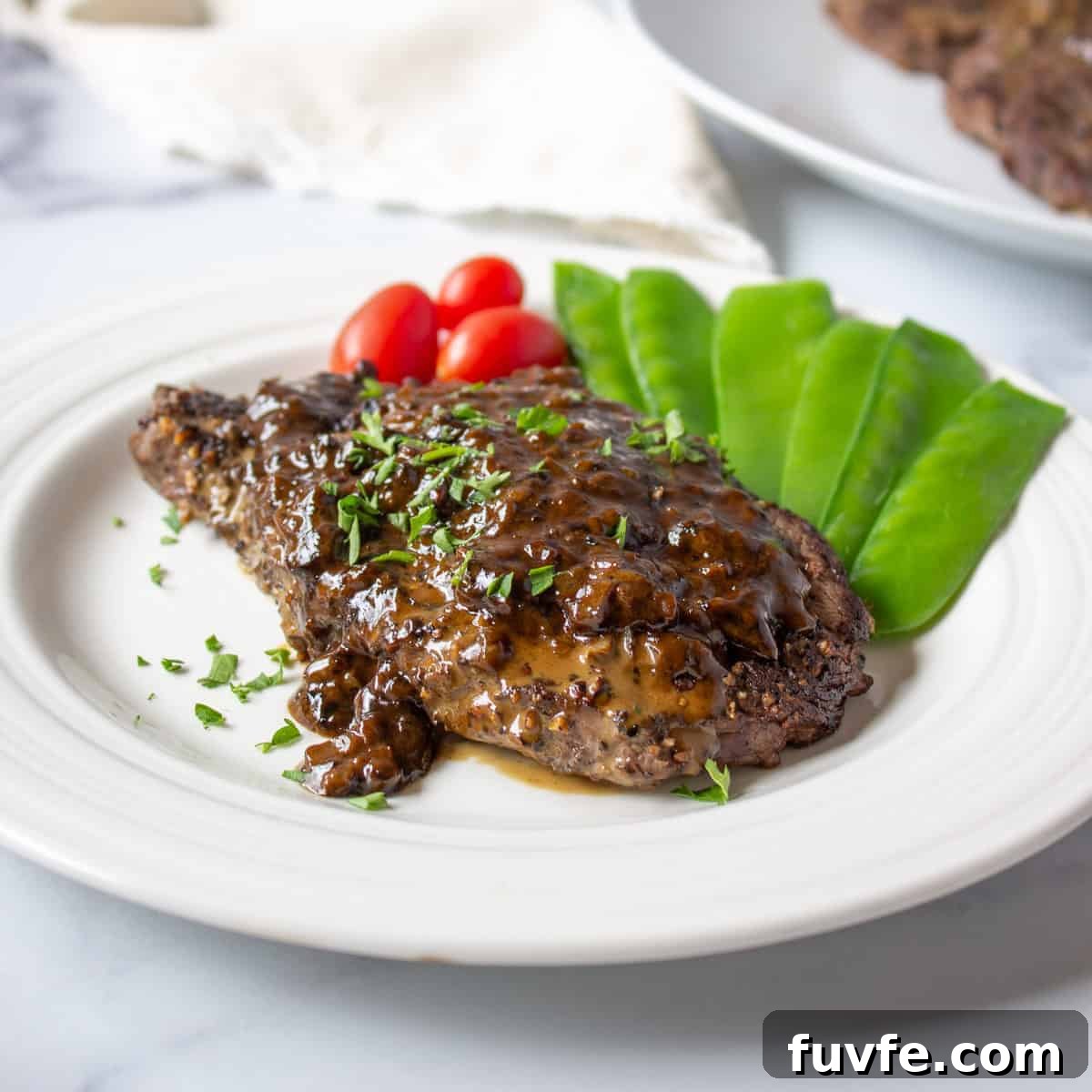 Elk Steak au Poivre Recipe: Peppercorn-Crusted Venison Steak 2 Elk steak topped with a brown sauce and freshly chopped parsley.