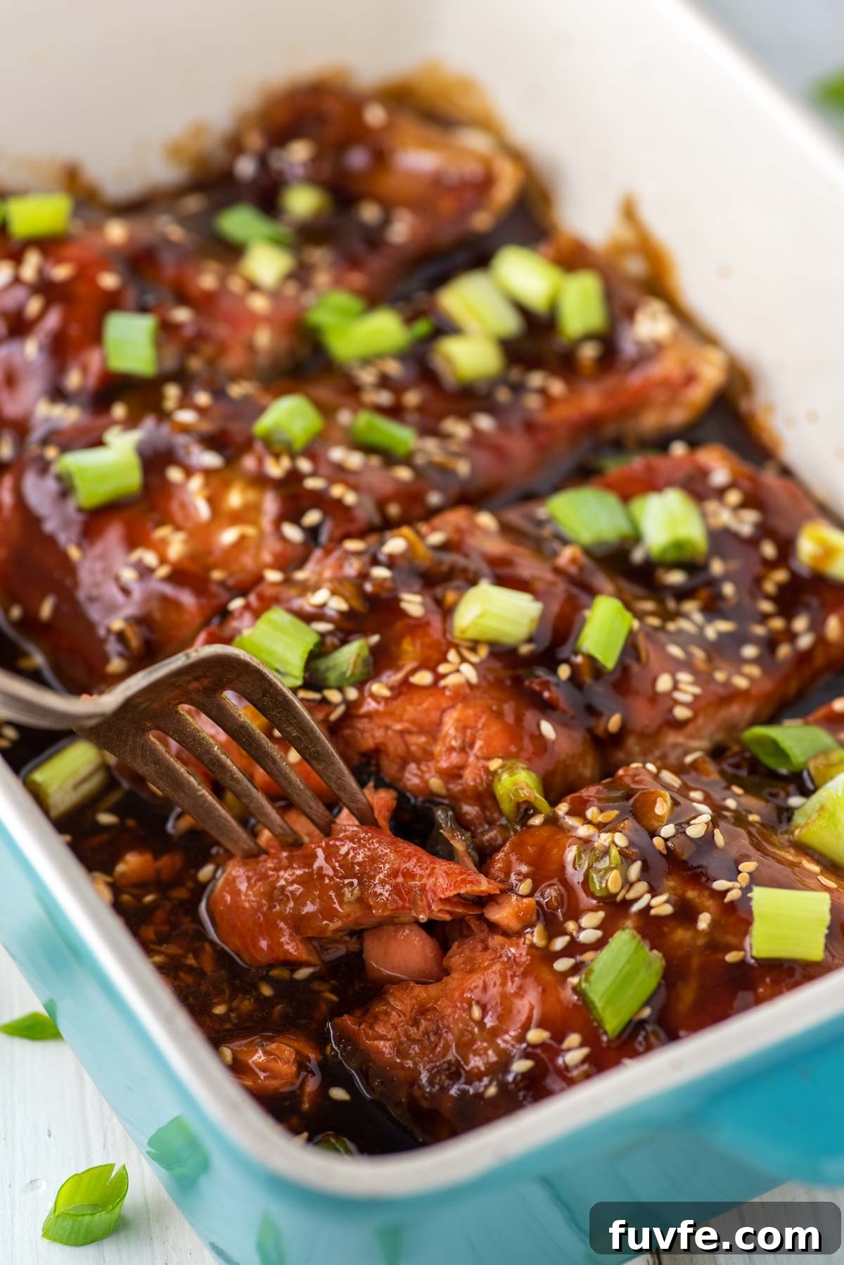 fork taking piece of teriyaki salmon out of dish