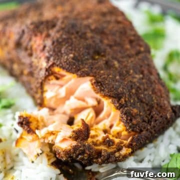 Fork cut into tandoori salmon on plate of white rice.
