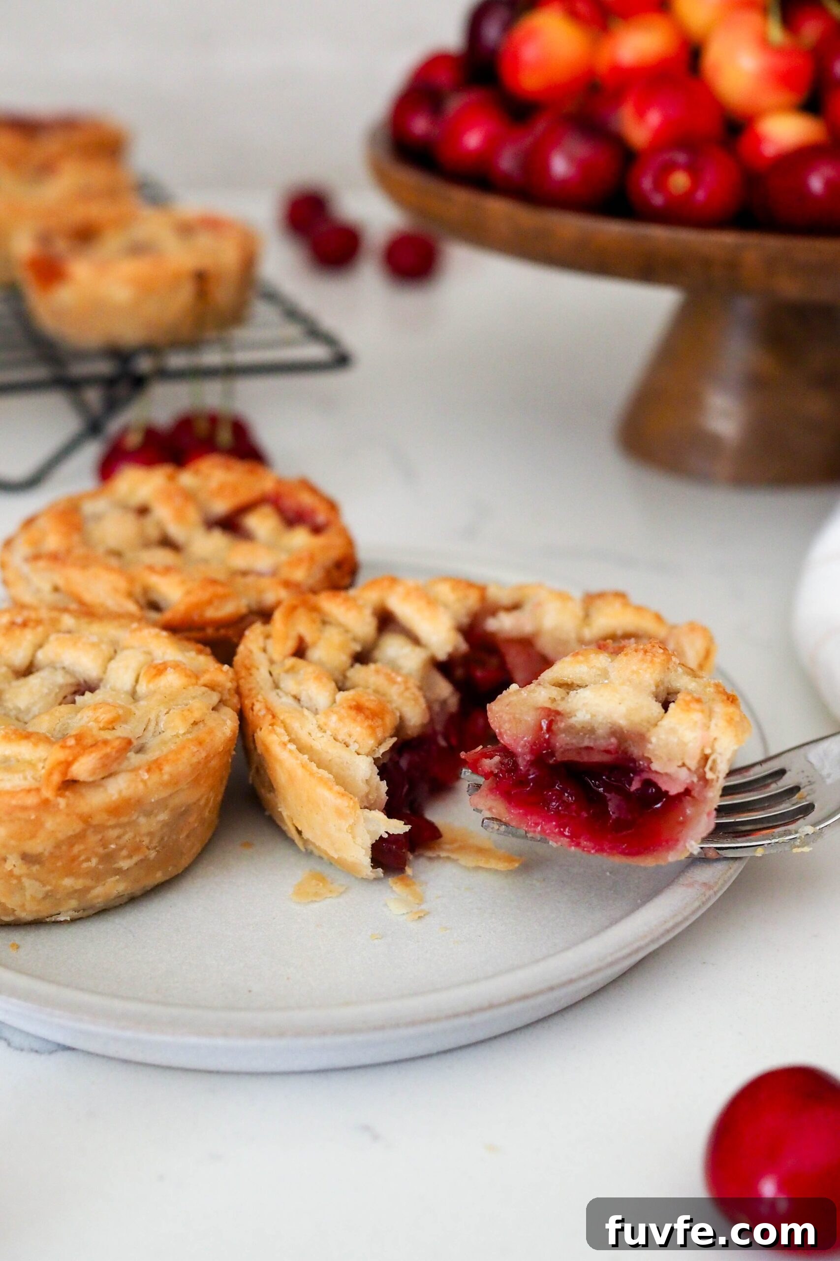 A fork pulls a piece of mini cherry pie off a plate.