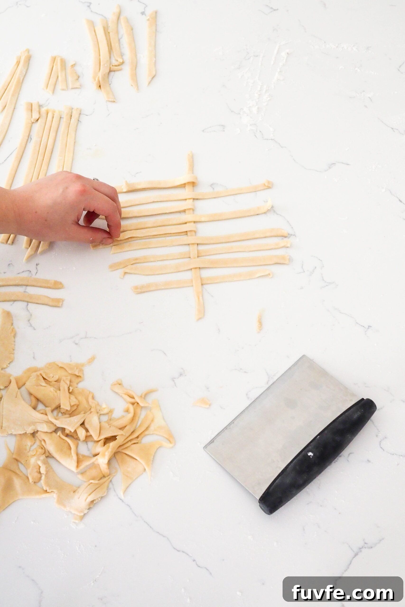 A hand makes the first lattice out of pie dough strips.