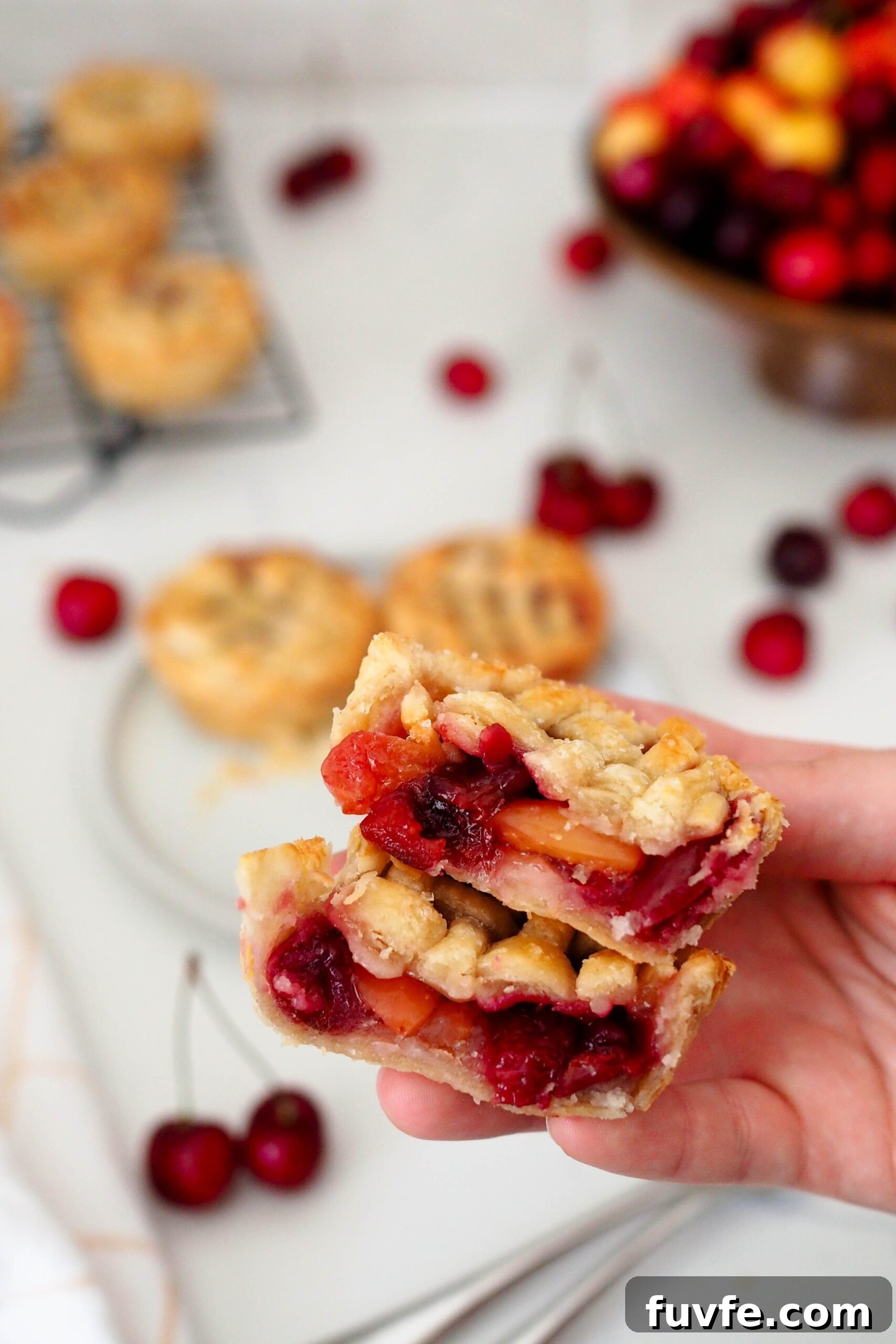 A hand holds up two halves of a mini cherry pie.