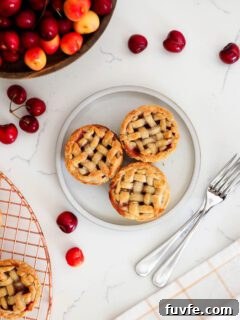 Three mini cherry pies on a plate with forks nearby.