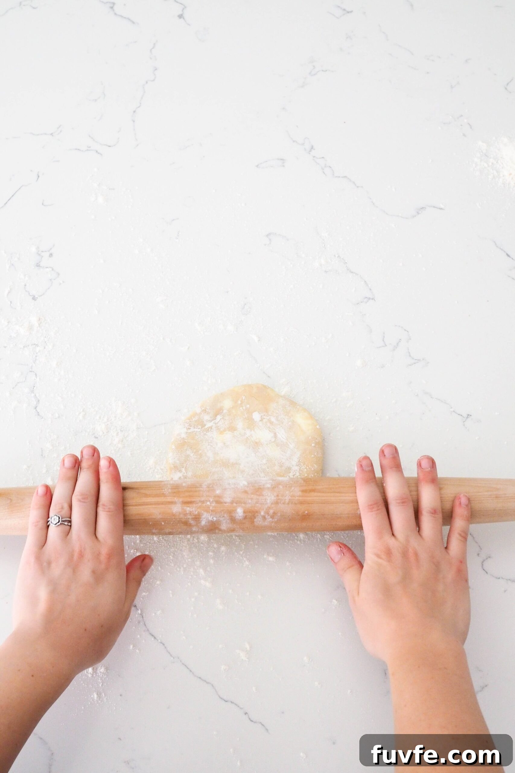 Two hands push a rolling pin over a pie crust.