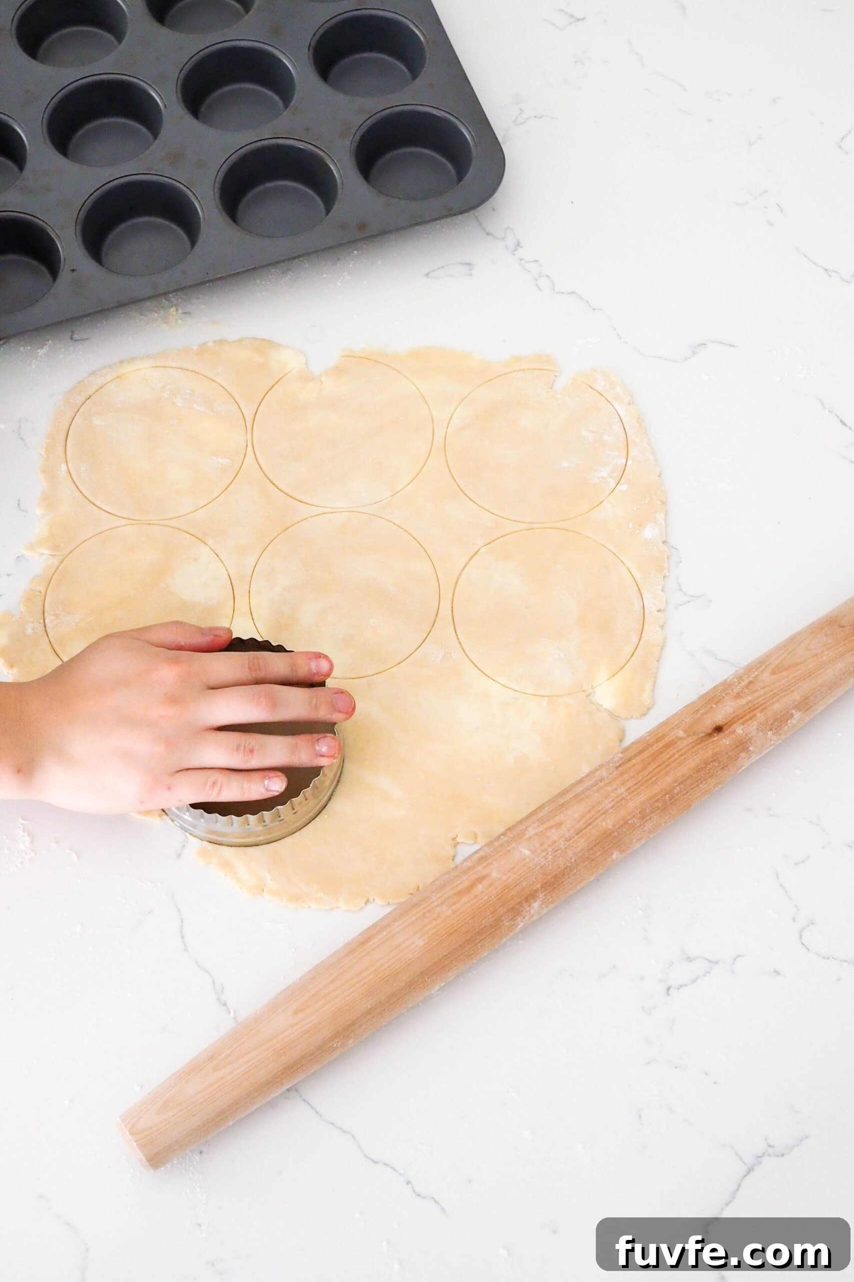 A hand cuts circles out of a rolled out pie crust.
