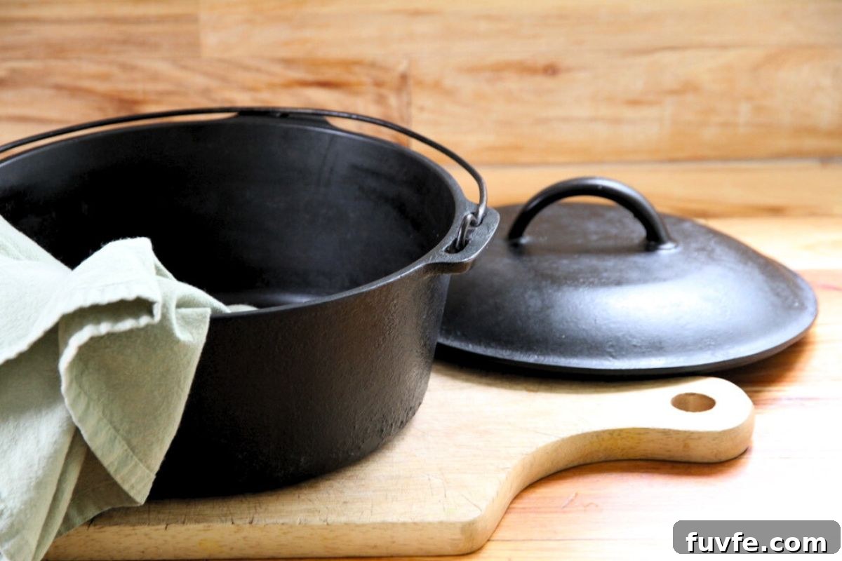 A black cast iron dutch oven and lid sitting on a wood cutting board and green tea towel.