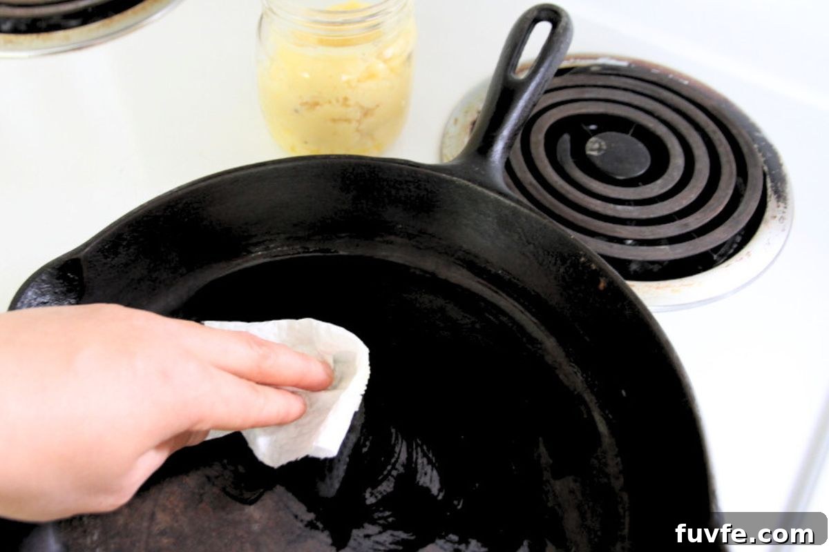 Wiping a warm cast iron skillet with paper towel and tallow fat. 