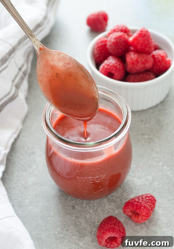 Raspberry dressing drizzling from a spoon into a jar.