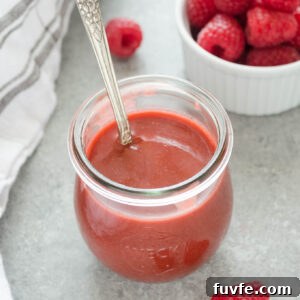 Raspberry vinaigrette dressing in a jar with a spoon buried inside.