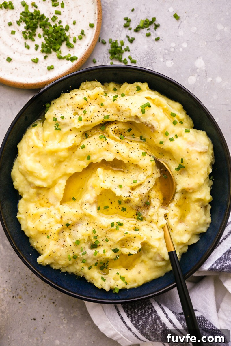 A small serving bowl filled with roasted garlic mashed potatoes sitting next to a plate of chopped chives
