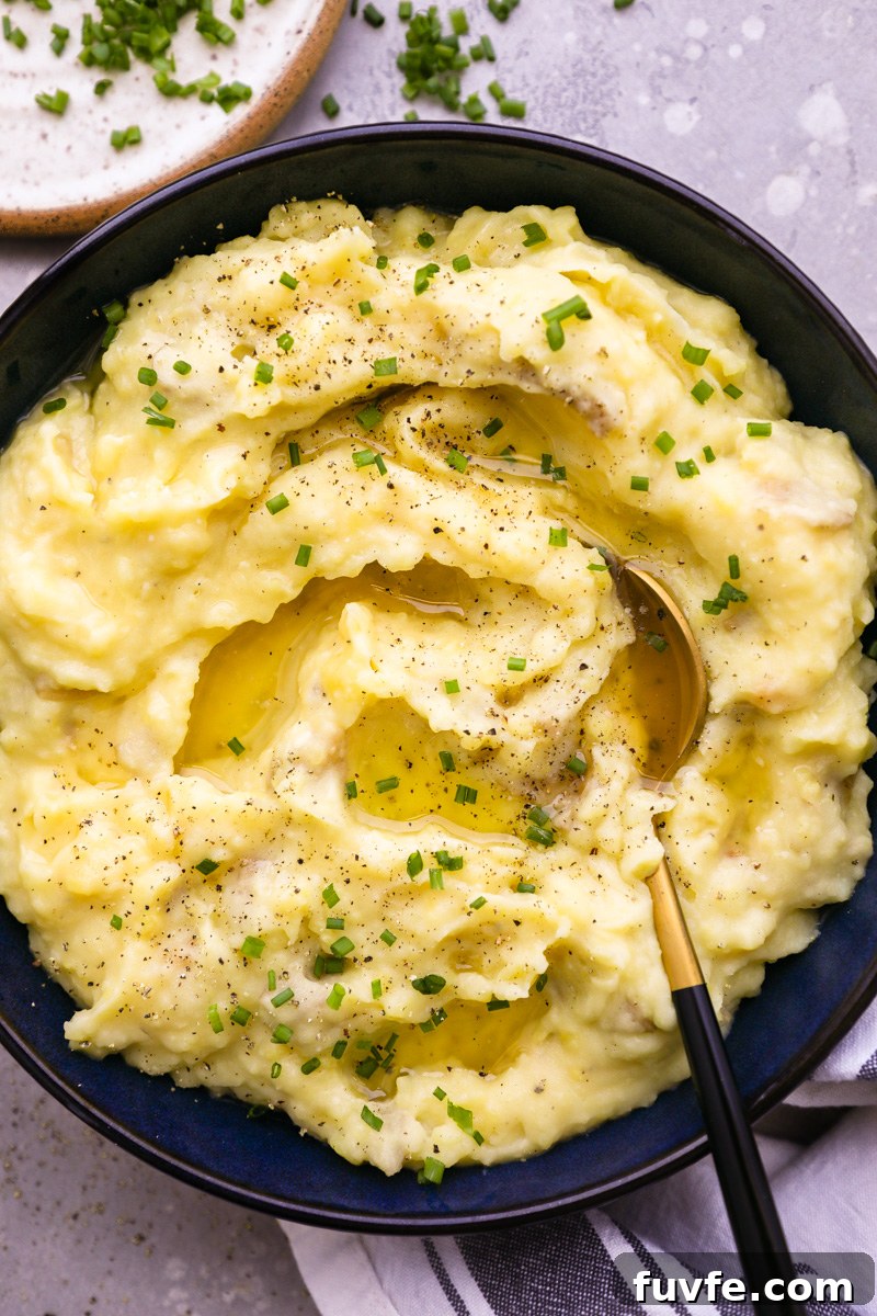A serving bowl filled with roasted garlic mashed potatoes with a spoon digging into it