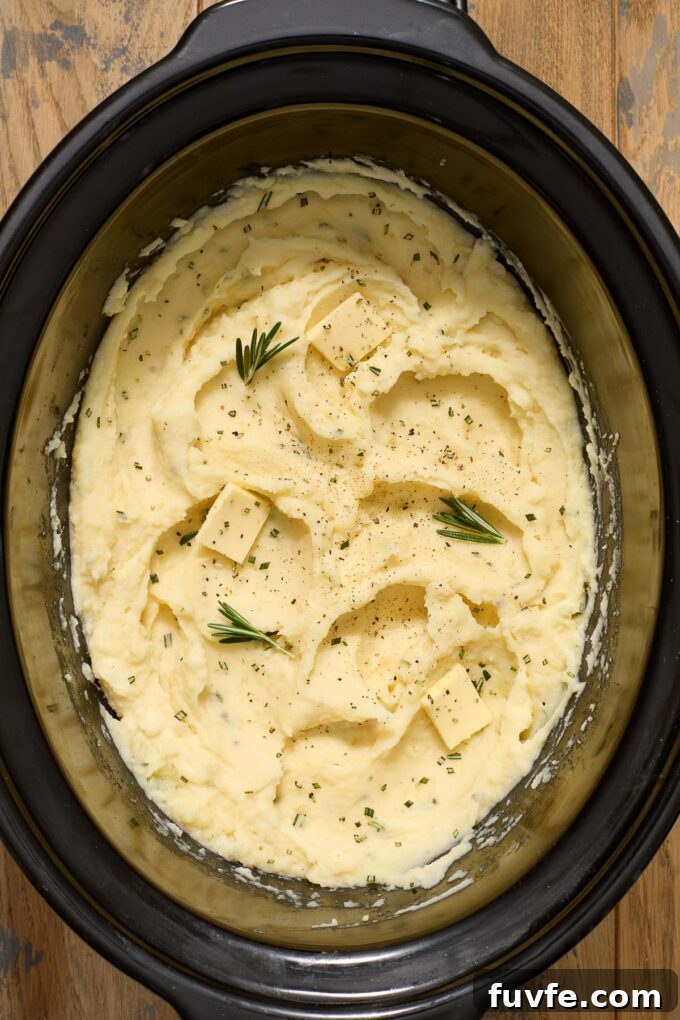 Buttermilk mashed potatoes in crock pot insert with rosemary and butter.