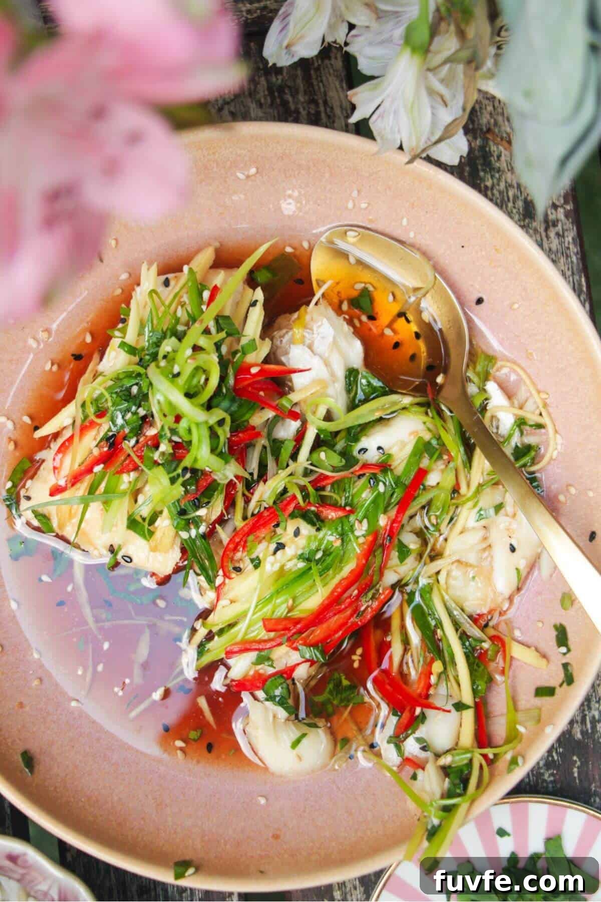 Two fish fillets topped with scallions, ginger and chili in a pink bowl.