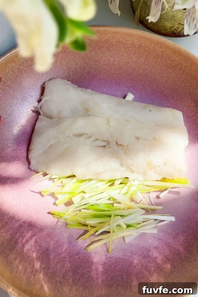 One piece of fish on top of sliced scallions in a pink bowl.