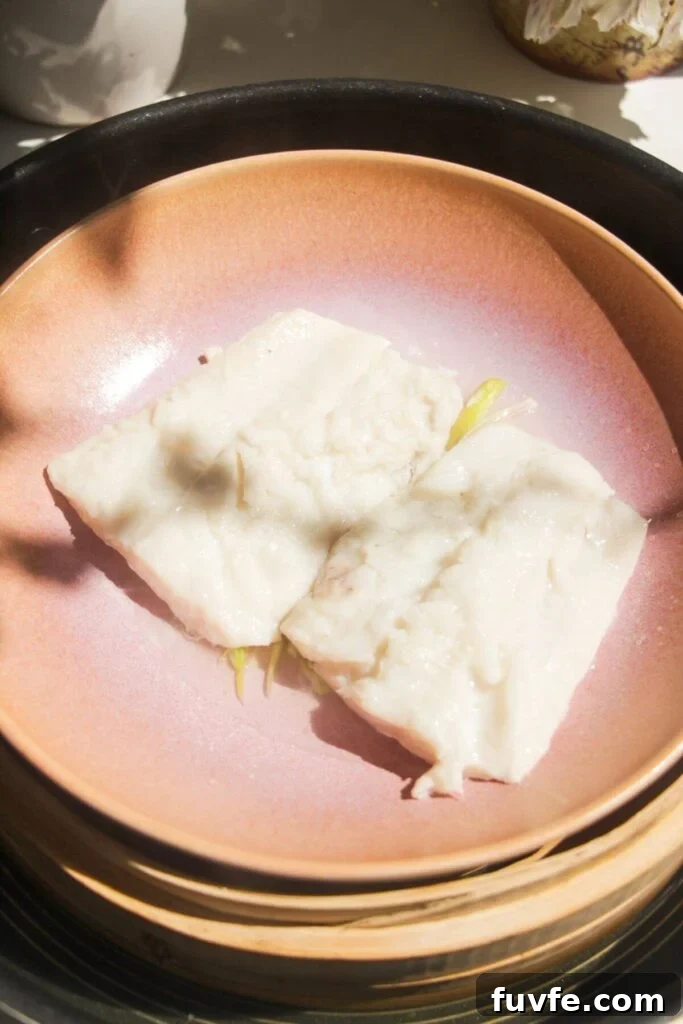 Two steamed fish fillets in a pink bowl in a steamer basket.