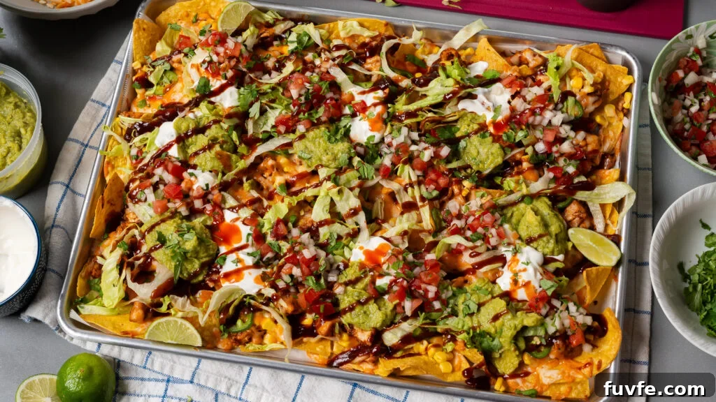 BBQ Rotisserie Chicken Nachos with Cheesy Jalapeño Topping 3 Loaded BBQ chicken nachos on a sheet pan with shredded cheese.