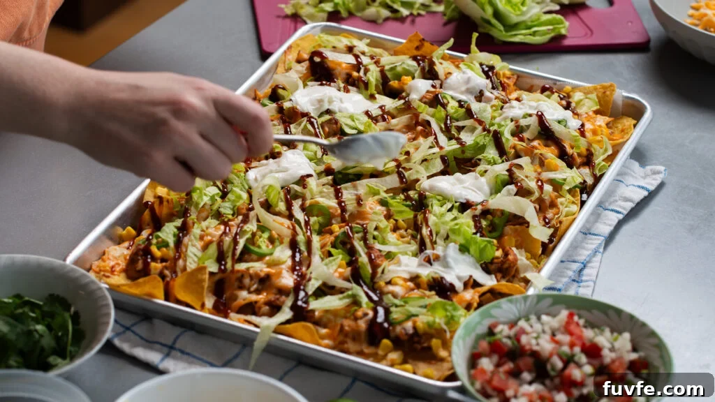BBQ Rotisserie Chicken Nachos with Cheesy Jalapeño Topping 6 Loaded BBQ chicken nachos on a sheet pan with shredded cheese.