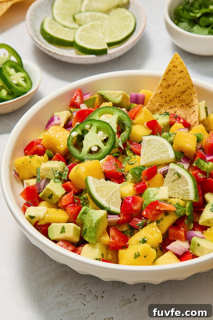 Mango and avocado salsa in a bowl with sliced lime and jalapeno.