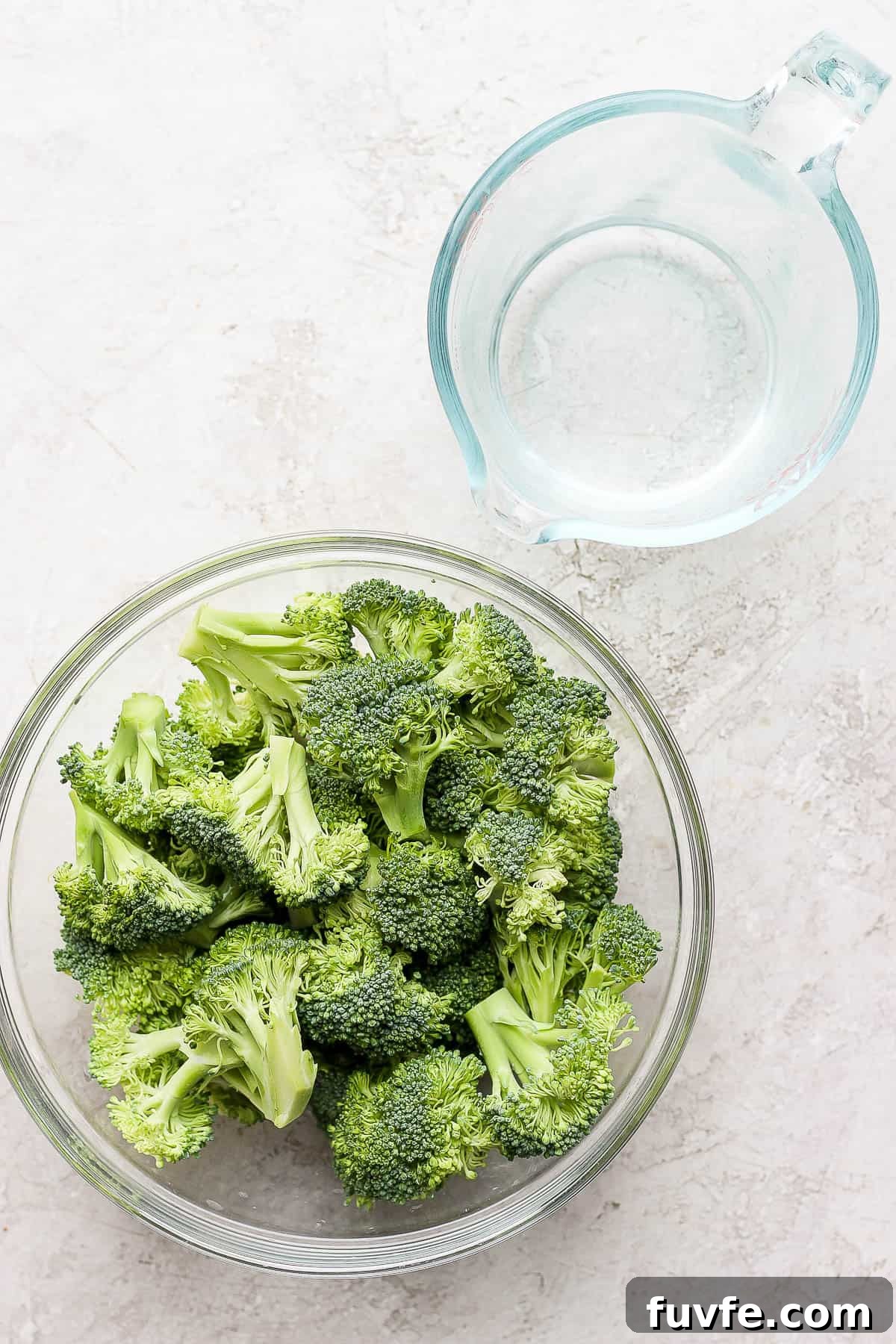 How to Steam Broccoli: Stovetop and Microwave Methods 3 Broccoli in a bowl and a measuring cup with water.