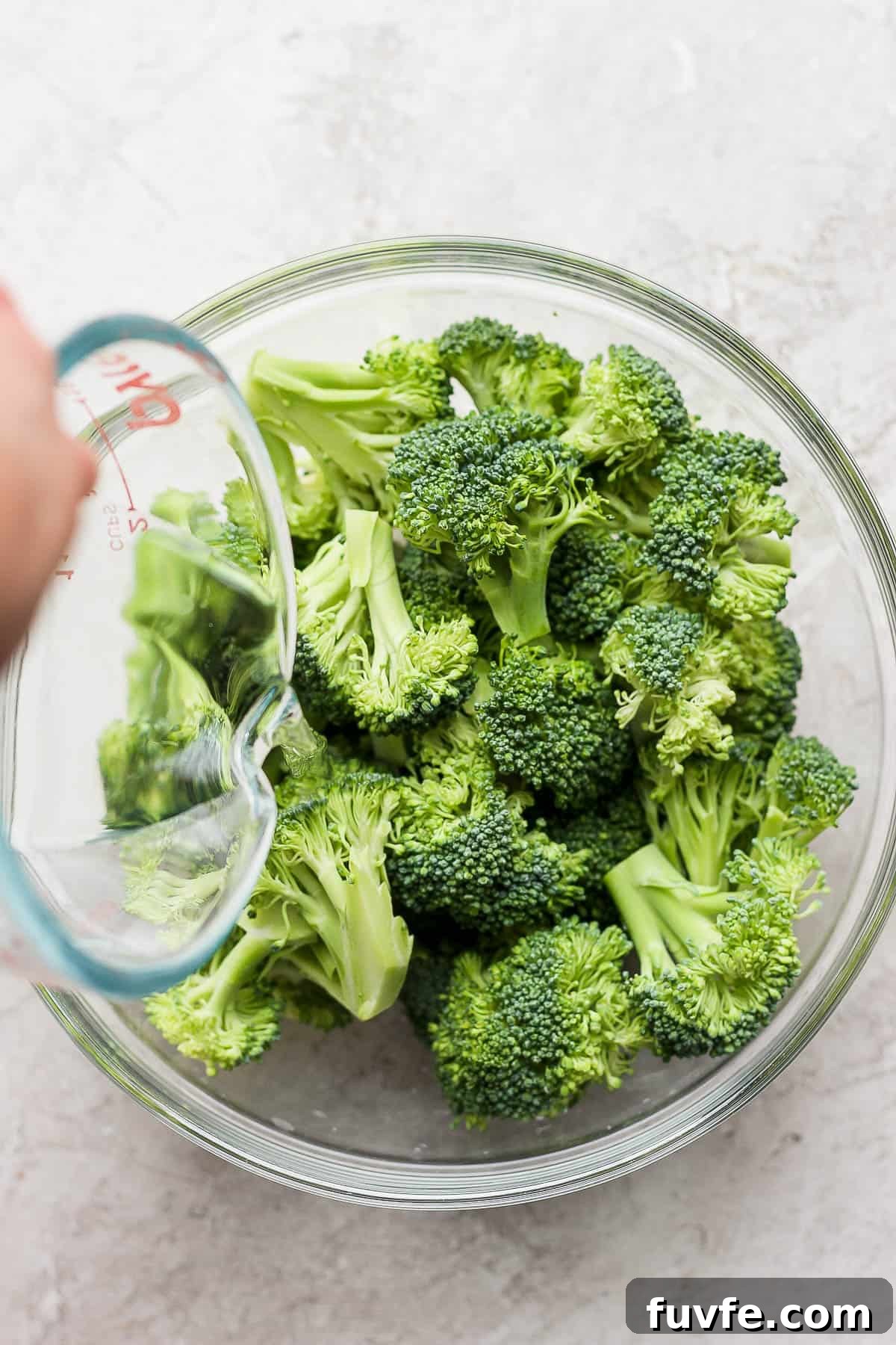 How to Steam Broccoli: Stovetop and Microwave Methods 8 Water being poured into a microwave safe bowl with broccoli in it.