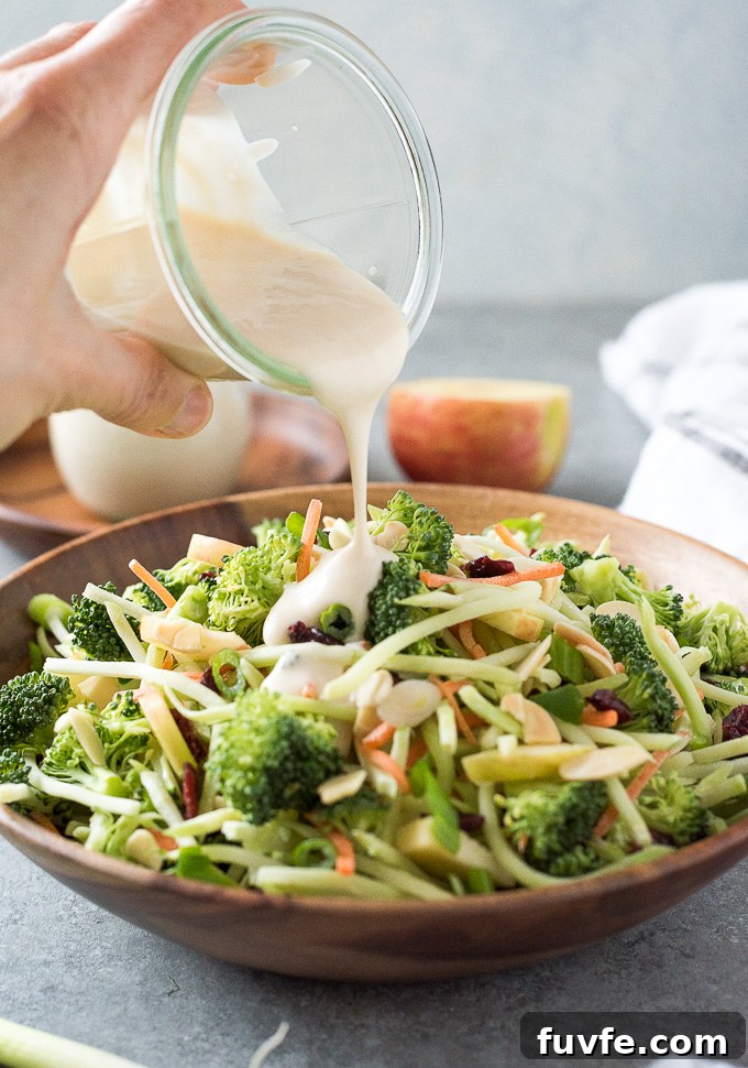 Broccoli Slaw in a bowl with dressing pouring over the top