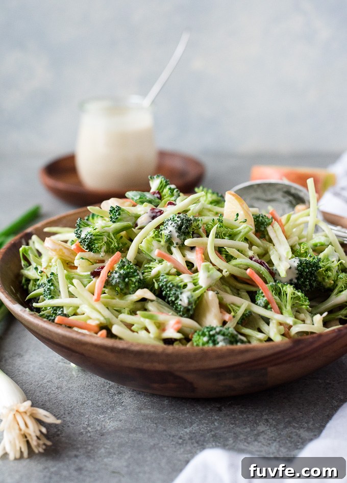 Bowl of broccoli slaw with serving spoon and coleslaw dressing nearby