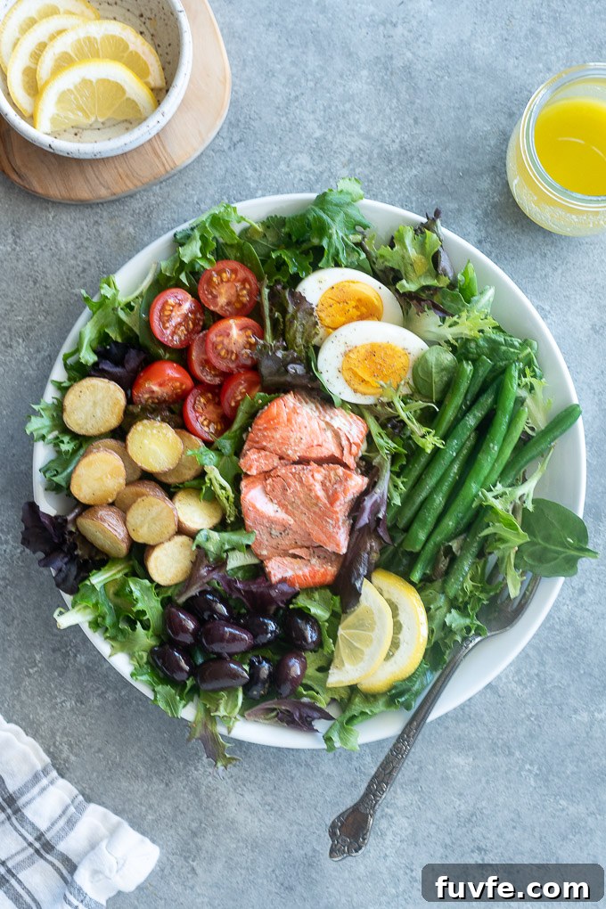 Salmon nicoise salad on a white plate with lemon slices and a fork