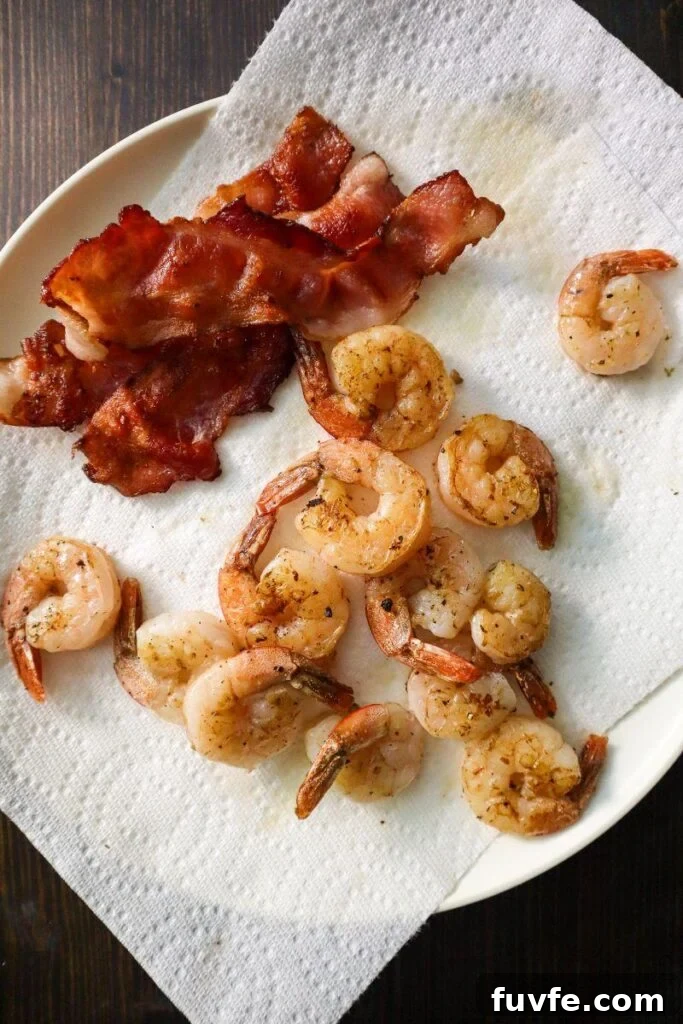 Crispy bacon and cooked shrimp on a white paper towel lined plate. 