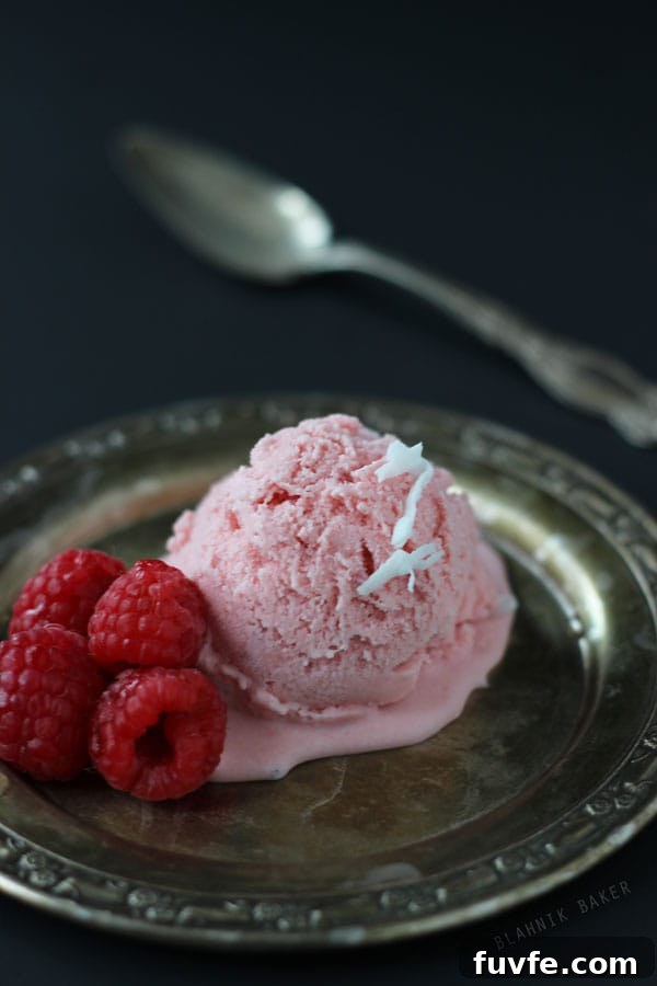 A scoop of rhubarb ice cream with fresh raspberries on a dark plate.