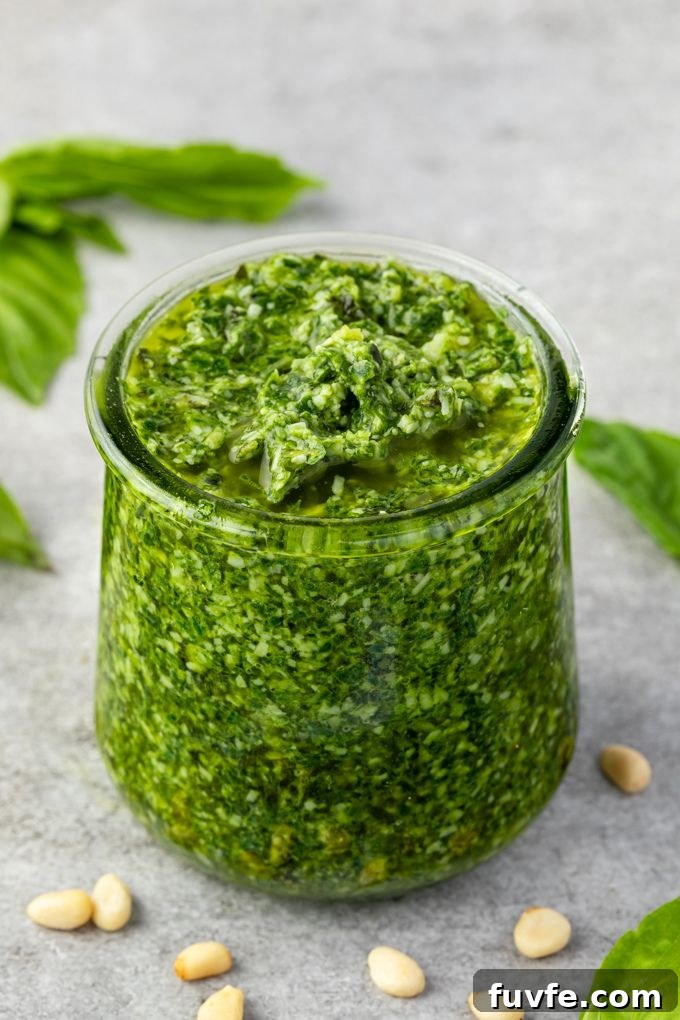 Basil pesto in a jar with pine nuts and basil leaves around it