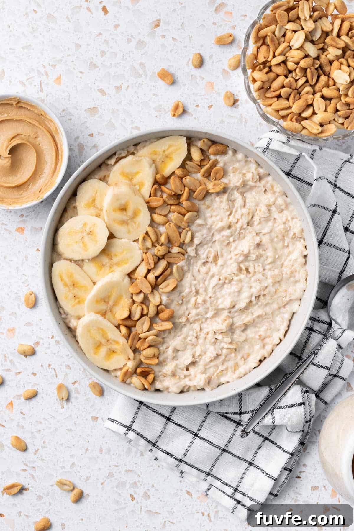 Bowl of Peanut Butter Porridge decorated with some banana slices and peanuts, sitting on a black and white tea towel.