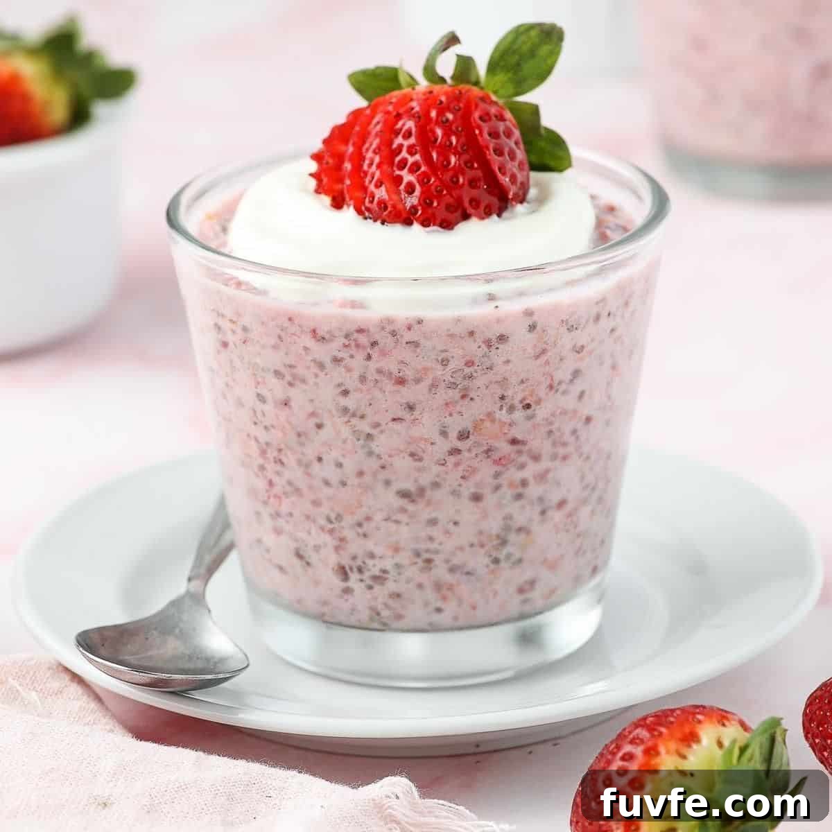 Glass jar of strawberry overnight oats, topped with yoghurt and a strawberry, sitting on a white saucer with a spoon on edge.