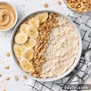 Bowl of Peanut Butter Porridge decorated with some banana slices and peanuts, sitting on a black and white tea towel.