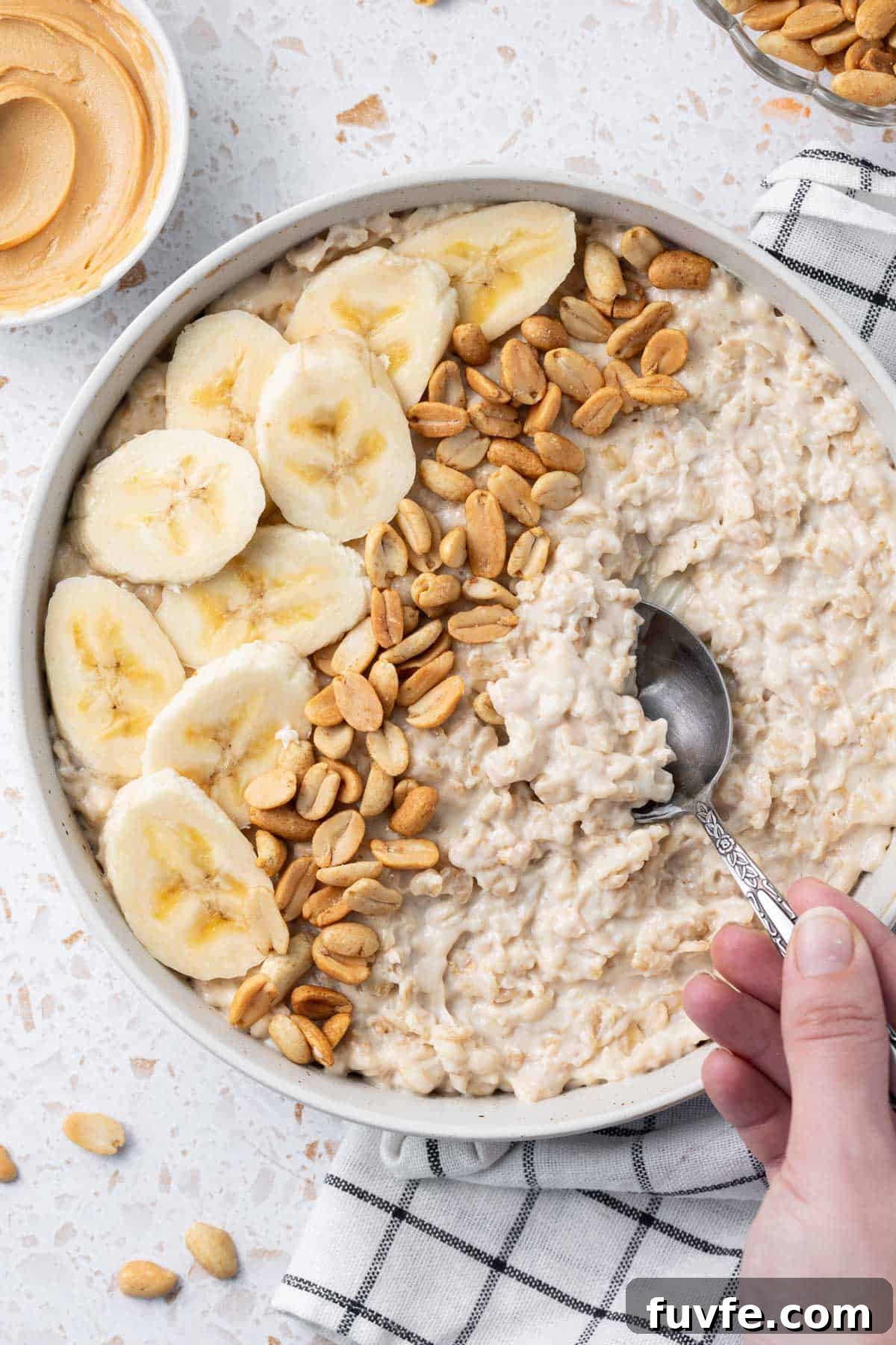 Bowl of Peanut Butter Porridge decorated with some banana slices and peanuts, with a spoon scooping some porridge.