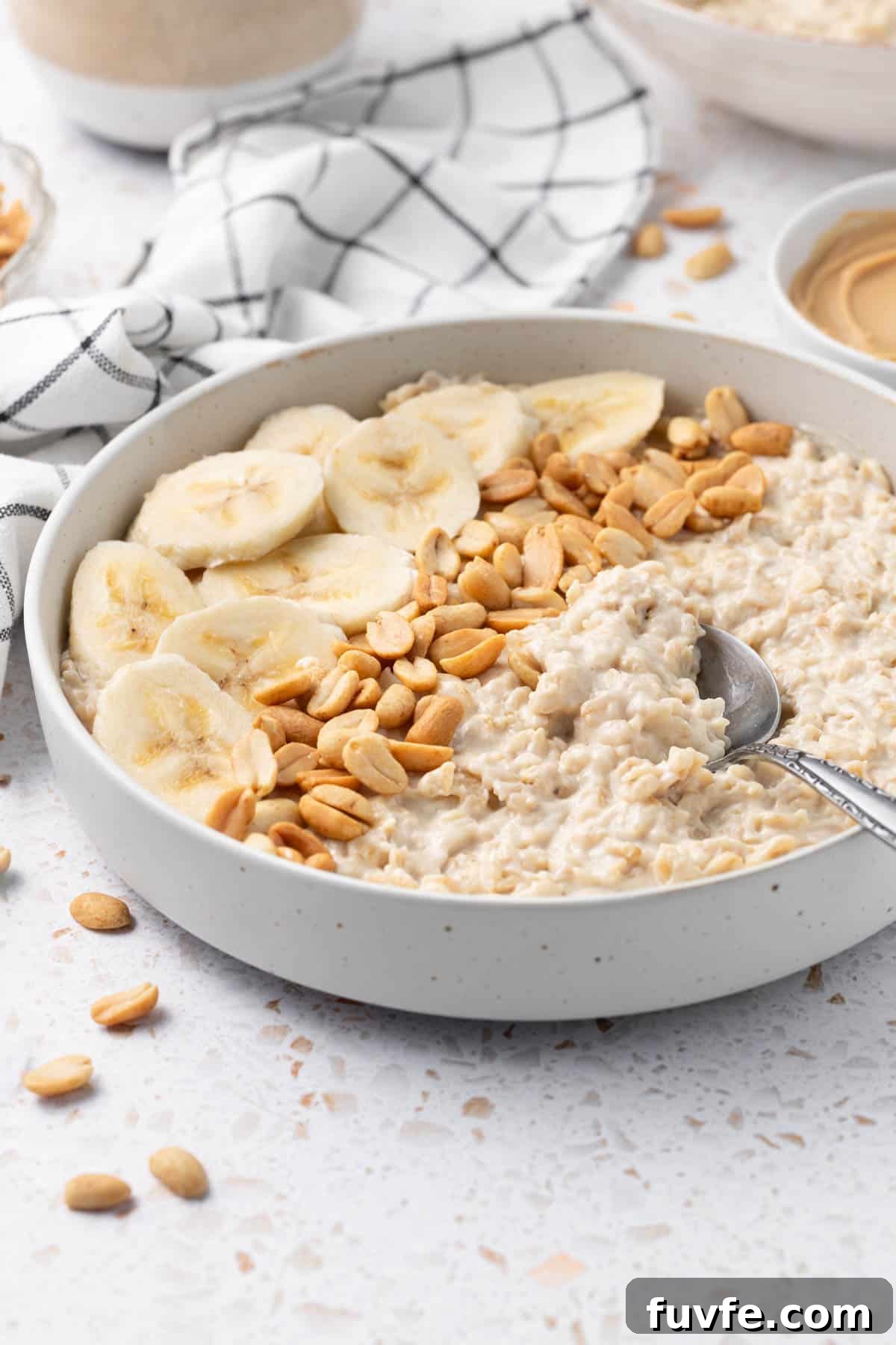 Bowl of Peanut Butter Porridge decorated with some banana slices and peanuts, with a spoon scooping some porridge.