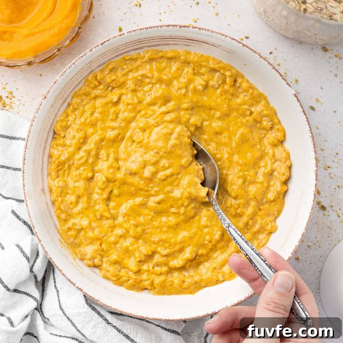 Round white bowl of pumpkin porridge with a spoon scooping up some of the mixture.