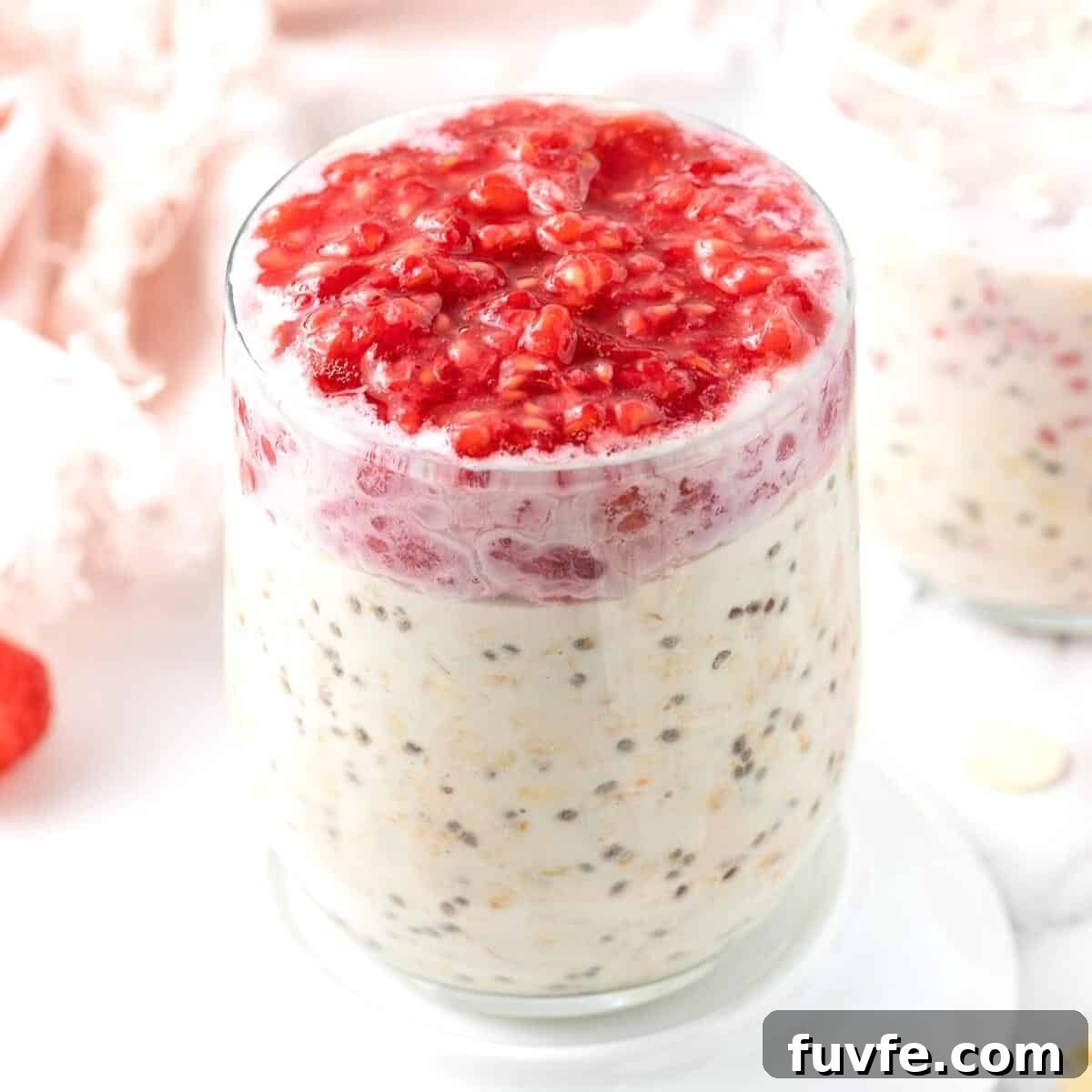 Glass jar of overnight oats topped with mashed raspberries, sitting on a white saucer.