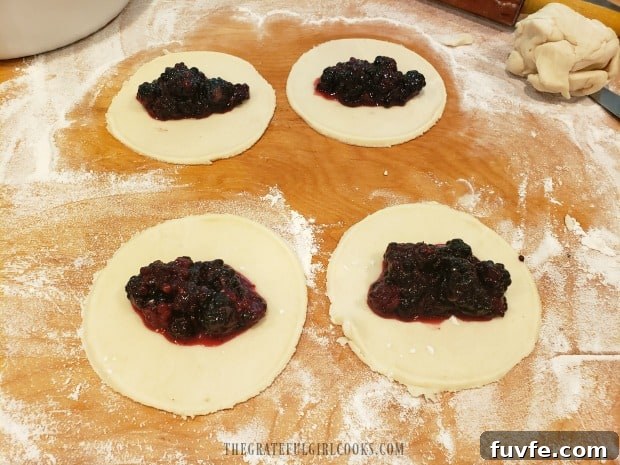 A spoonful of blackberry pie filling is placed onto each pie dough circle.