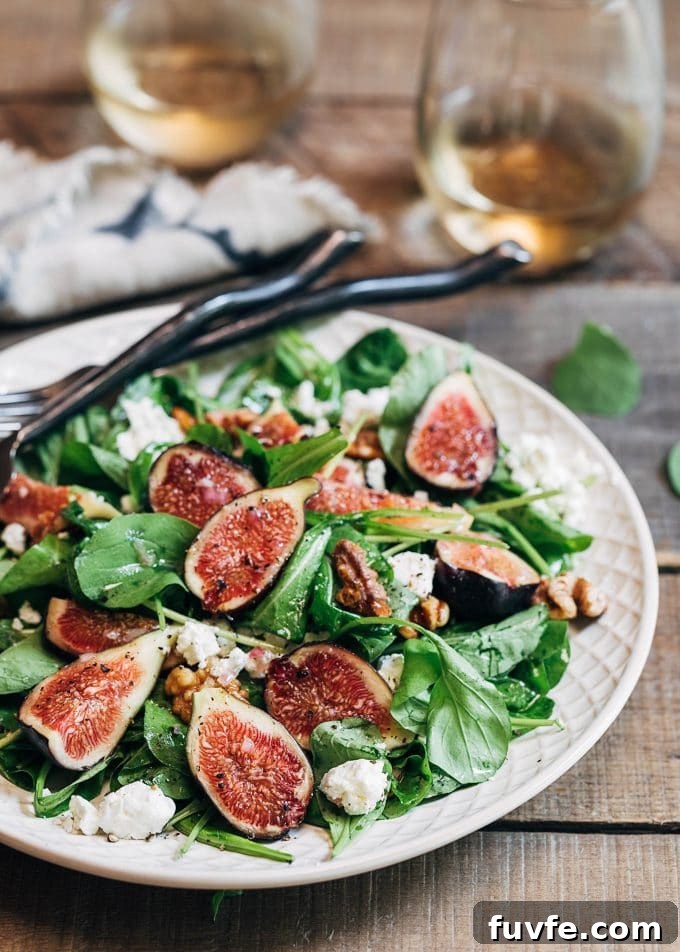 A fresh fig salad on a large white plate. Two glasses of wine rest in the background.